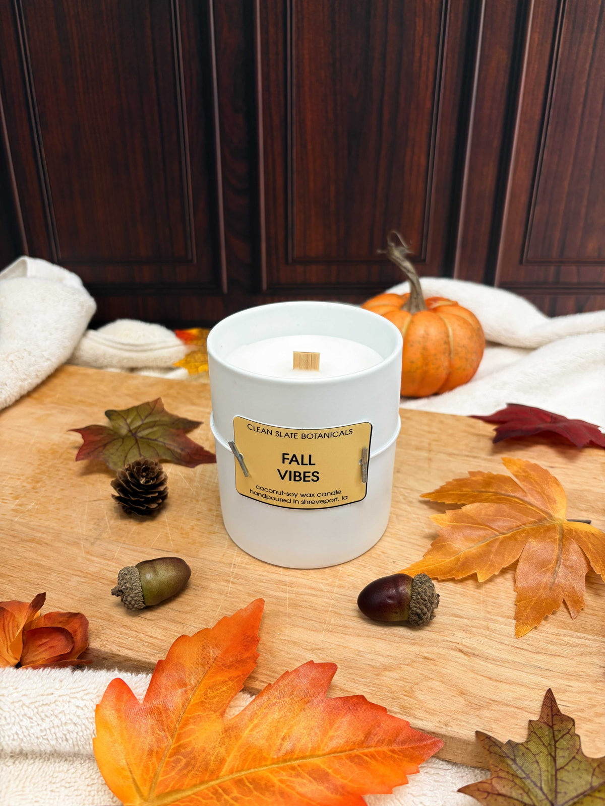 Fall Vibes Candle in a white glass jar with a tan label and single wooden wick, styled with autumn leaves and acorns