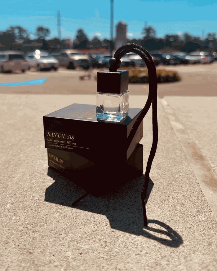 Santal 318 Car Diffuser in a clear glass bottle with a dark cap and hanging cord, displayed with its black box