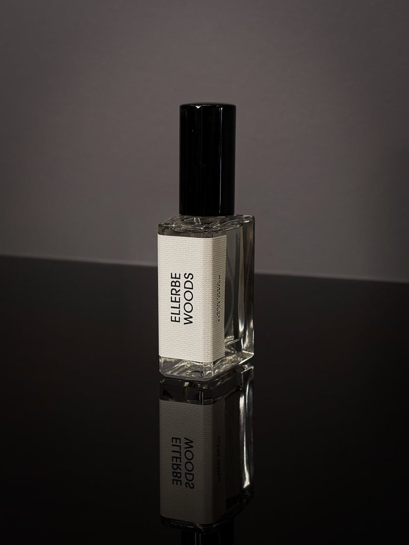 Ellerbe Woods Wearable Fragrance clear rectangular glass bottle with black cap and white label on a reflective black surface