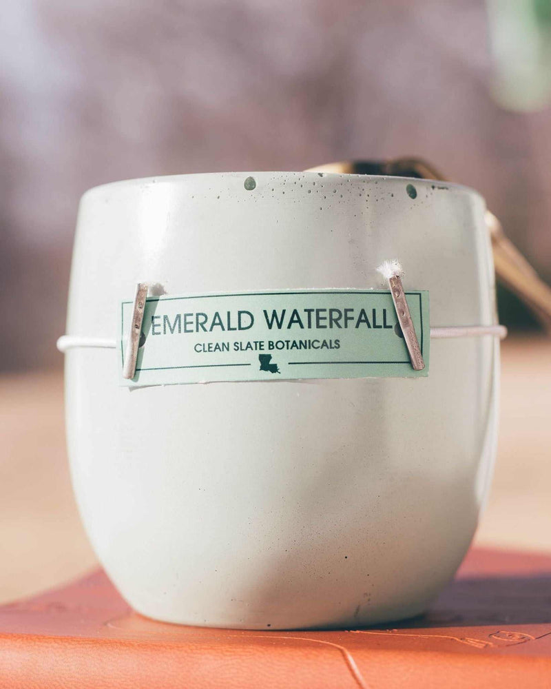 Emerald Waterfall Candle in a rounded cream-speckled concrete vessel with a green botanical label and two wicks