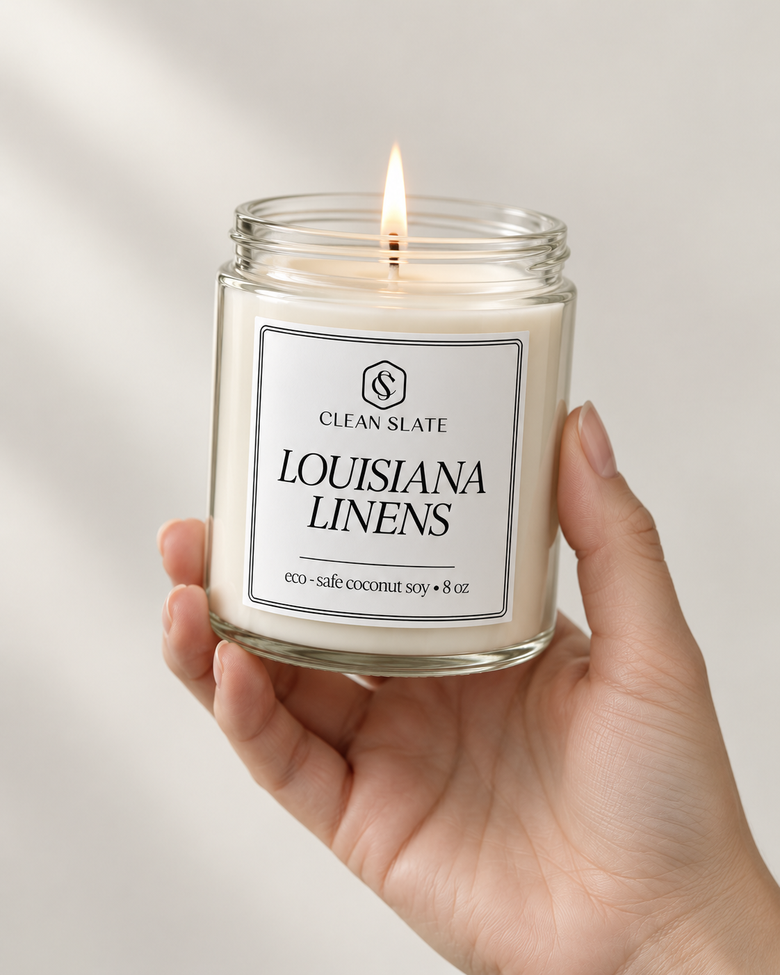 Fresh linen candle in a clear glass jar with white wax and a lit wick, featuring a minimalist black and white label