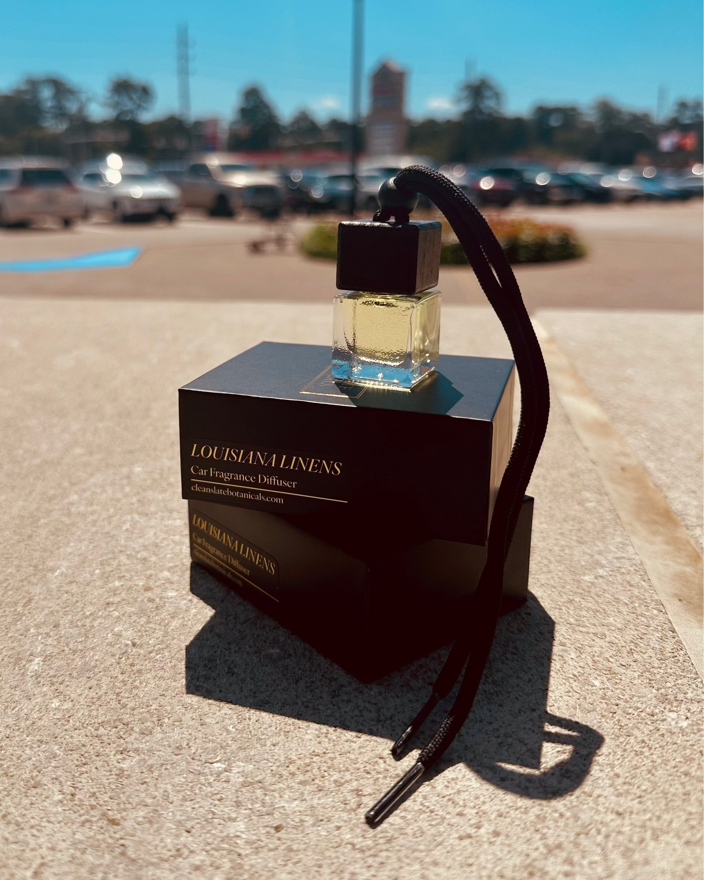 Louisiana Linens Car Diffuser in a clear glass bottle with pale yellow fragrance oil, dark cap and hanging cord beside its box