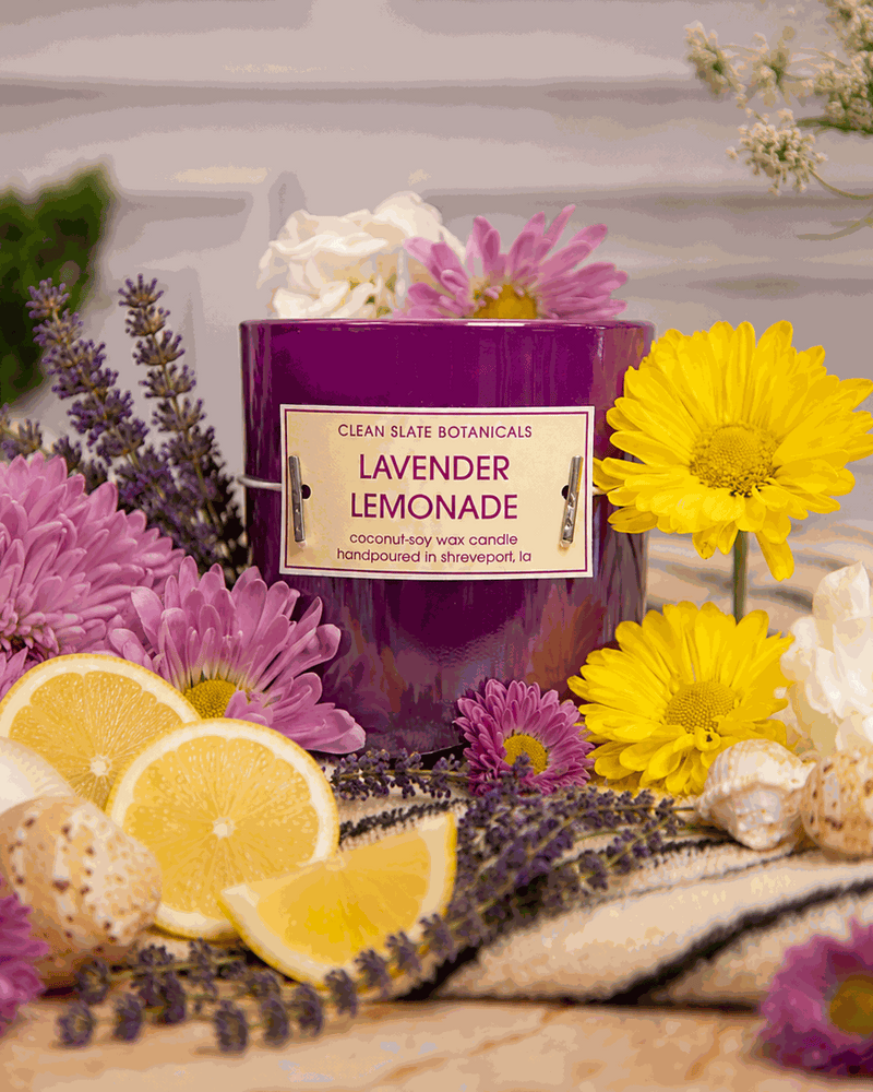 Lavender Lemonade candle in a glossy purple glass jar with a cream label, surrounded by lavender, flowers and lemon slices