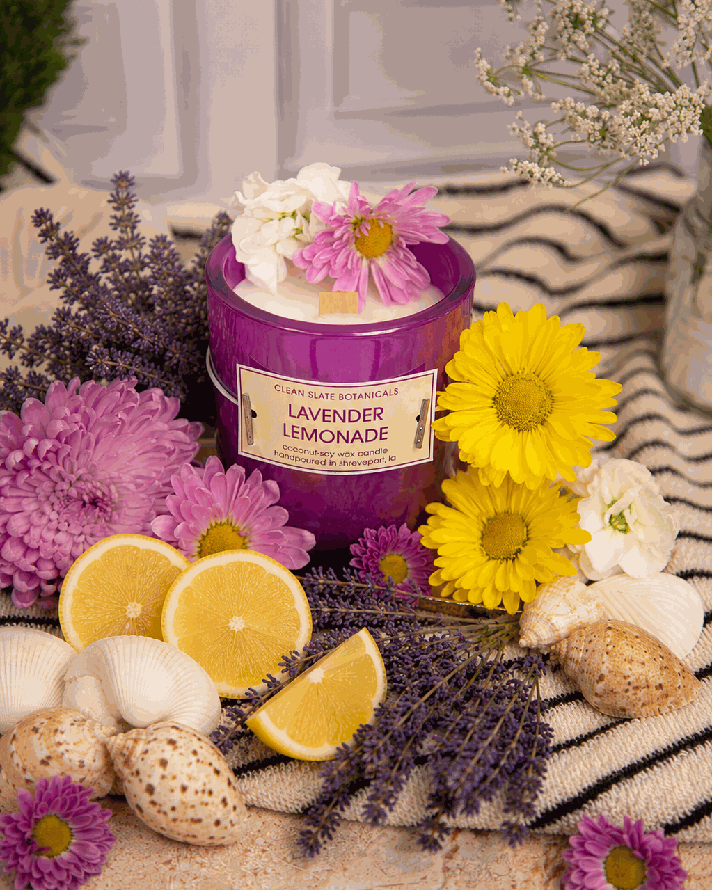 Lavender Lemonade candle in a glossy purple glass jar with a cream label, topped with pink and white flowers