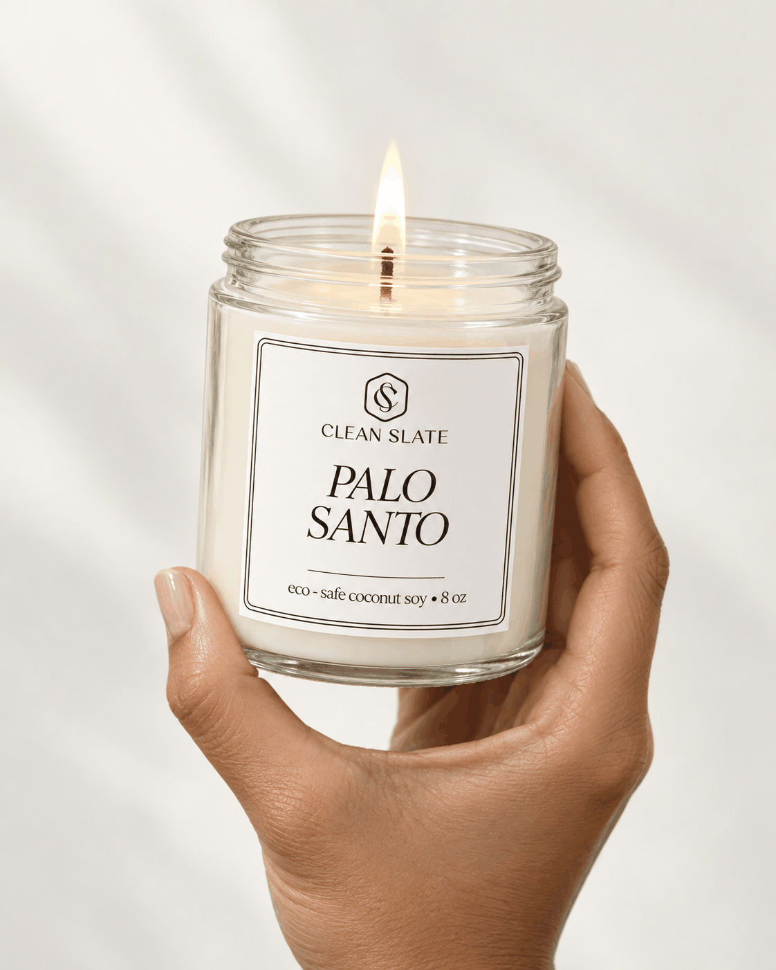 Palo Santo Candle in clear glass jar with white eco-safe coconut soy wax held by a hand with a lit flame