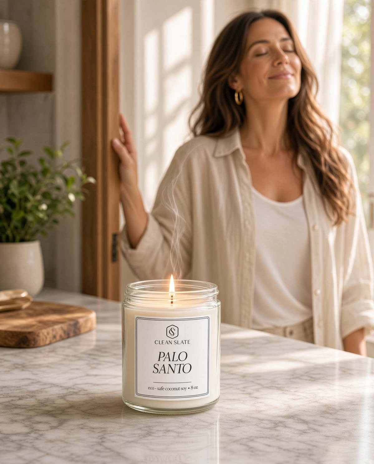 Palo Santo Candle in clear glass jar with white wax and minimalist label on marble countertop, woman enjoying scent nearby
