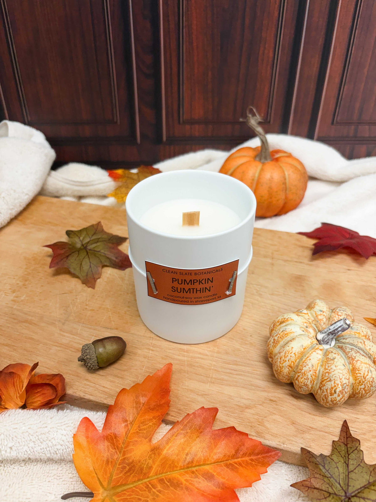 Pumpkin' Sumthin' Candle in a white ceramic jar with an orange label, wooden wick and pumpkin branding