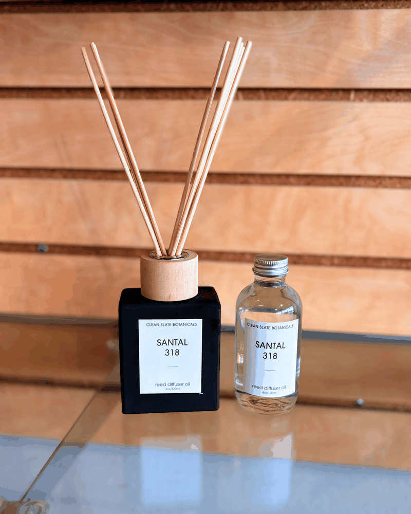 Santal 318 Reed Diffuser in a black square bottle with a pale wood collar and reeds, beside a clear glass refill bottle