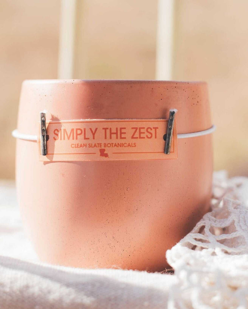 Simply The Zest Candle in a peach-pink speckled concrete vessel with a clear label and metal clips